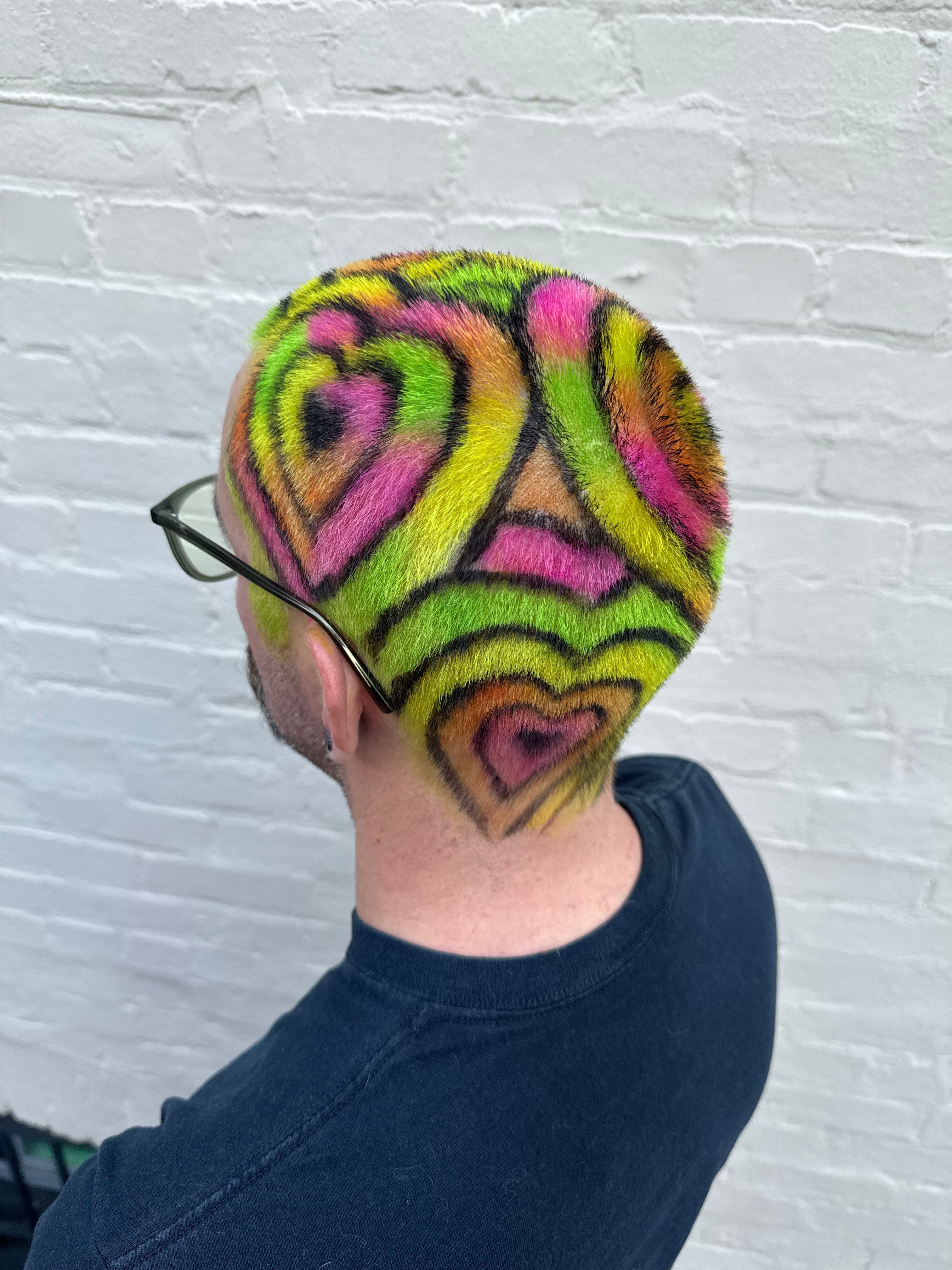 A client with shaved hair dyed neon green, pink, orange, and yellow with black heart outlines.